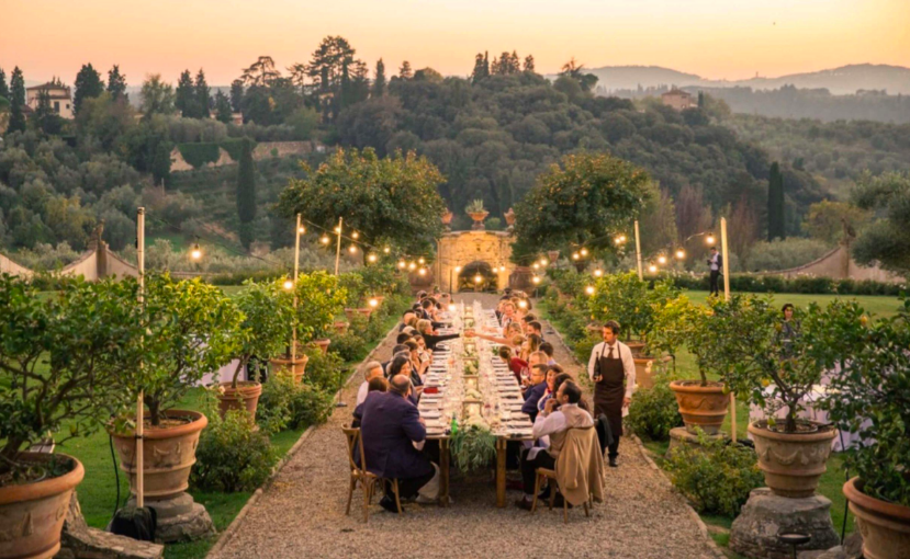 Lange dinertafel met lichtjes in een Italiaanse tuin bij zonsondergang